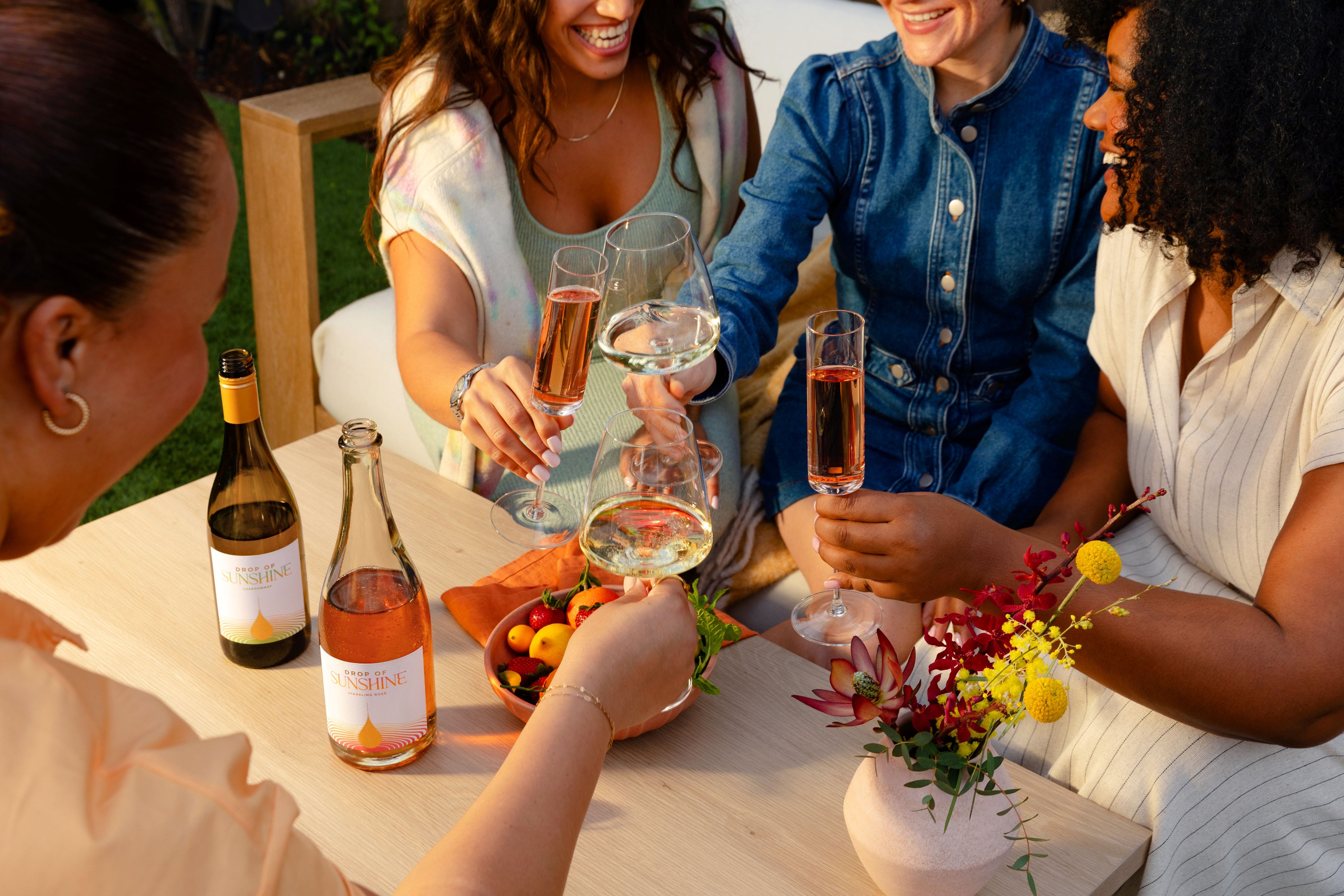 Four women sitting around a table each with a glass of wine celebrating by bringing their glasses together in a manner to cheers